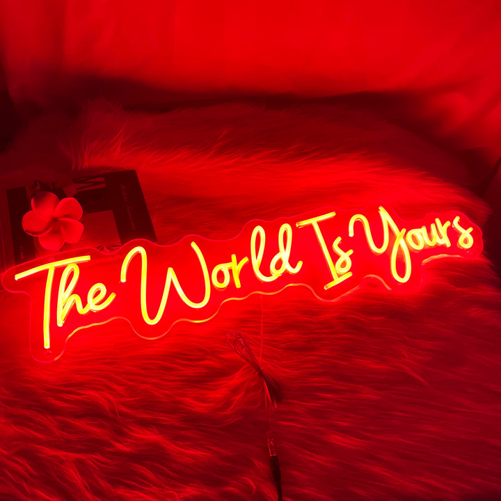 A vibrant SELICOR neon sign displaying the words The World is Yours in bold glowing letters against a dark background